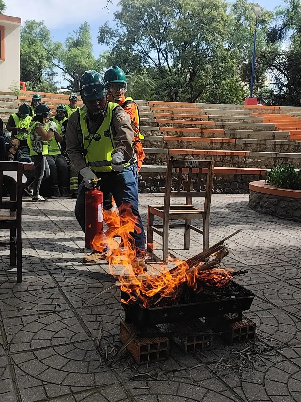Voluntario con casco verde y chaleco reflectivo ataca el fuego con un extintor durante el simulacro CERT
