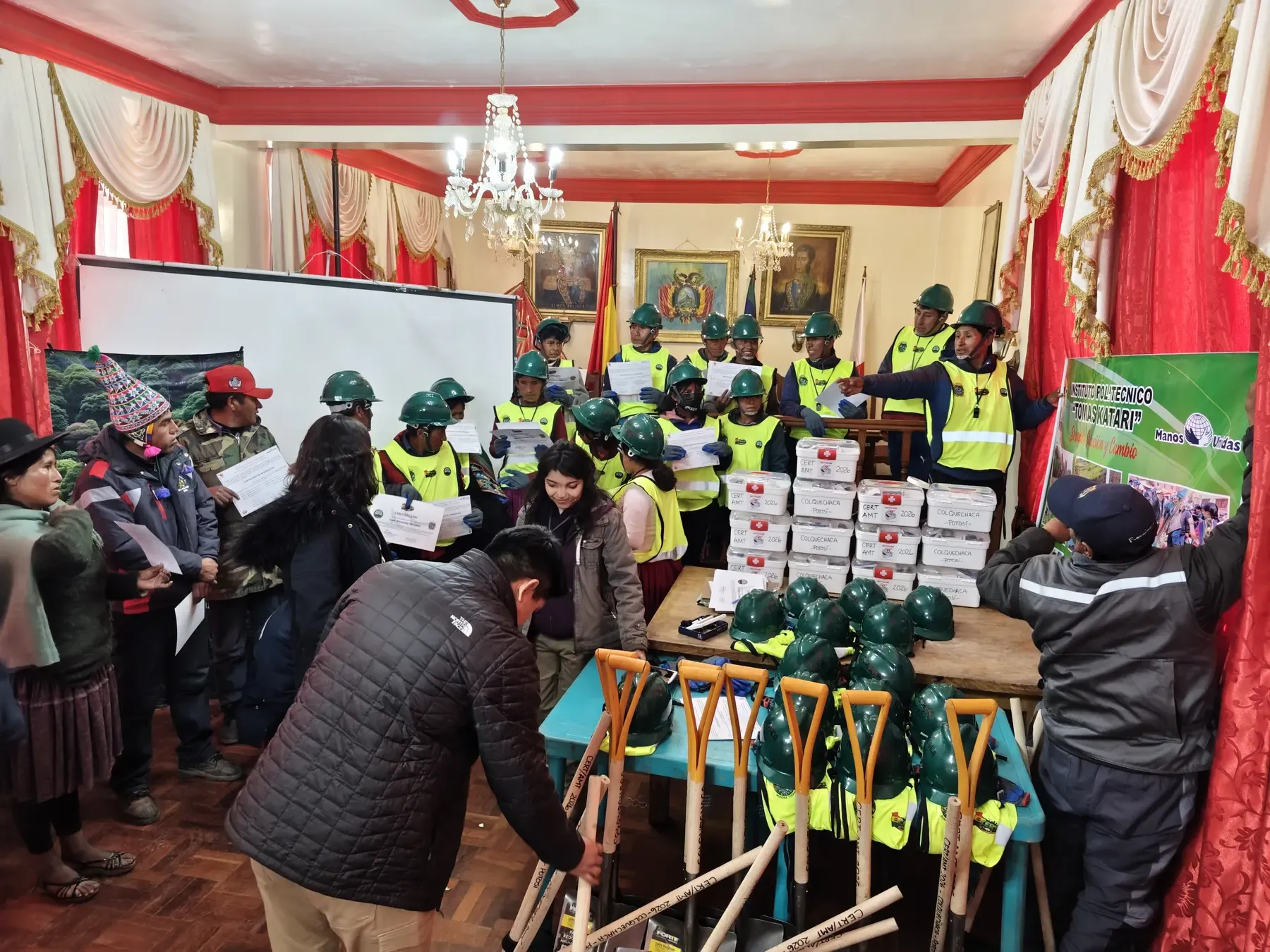 Brigadistas CERT con cascos verdes y chalecos muestran sus certificados junto a botiquines, cascos y palas rotuladas CERT AMT 2026 en Colquechaca, Potosí