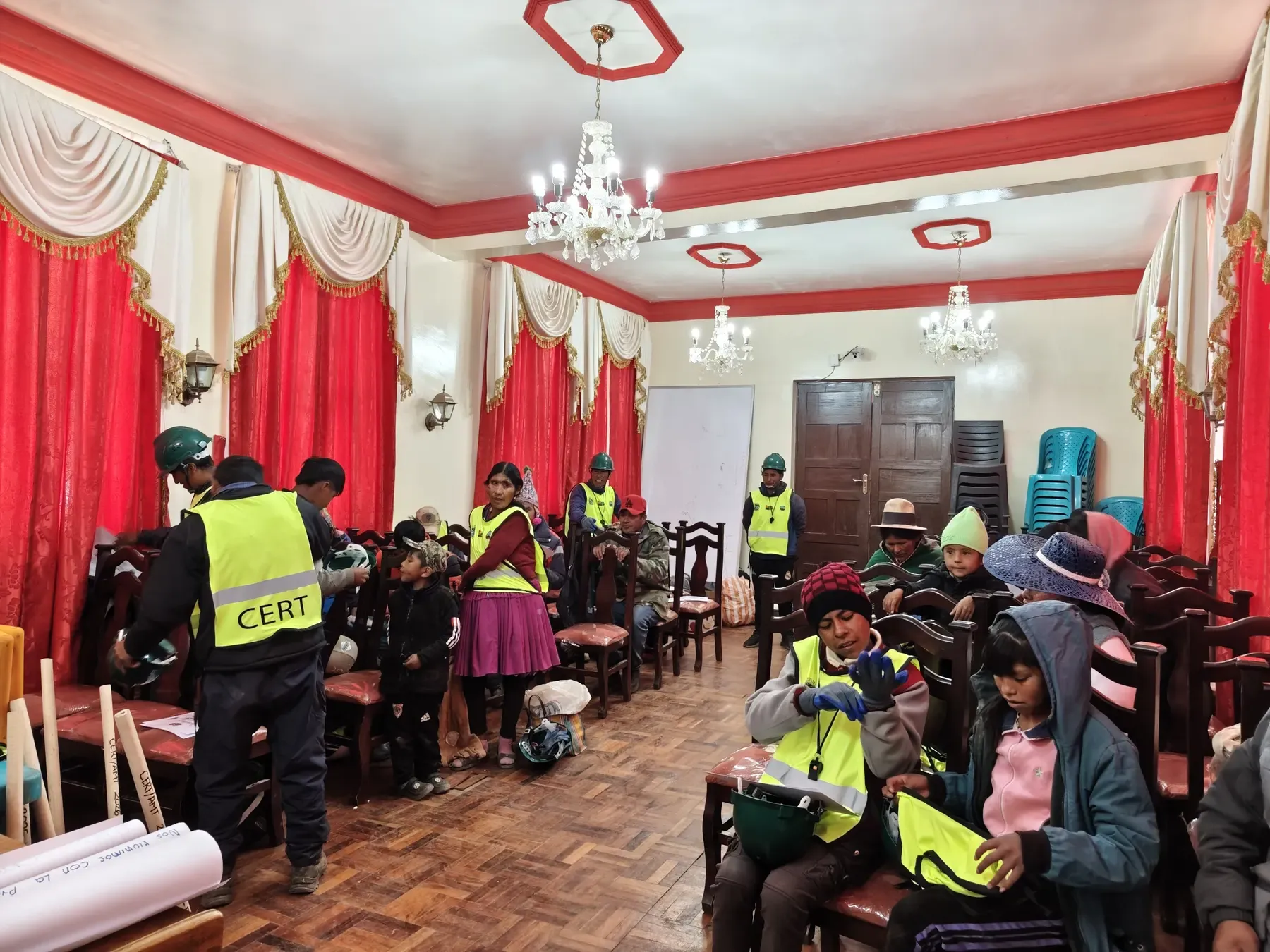 Participantes se colocan cascos verdes, guantes y chalecos reflectivos CERT en el salón comunal de Colquechaca