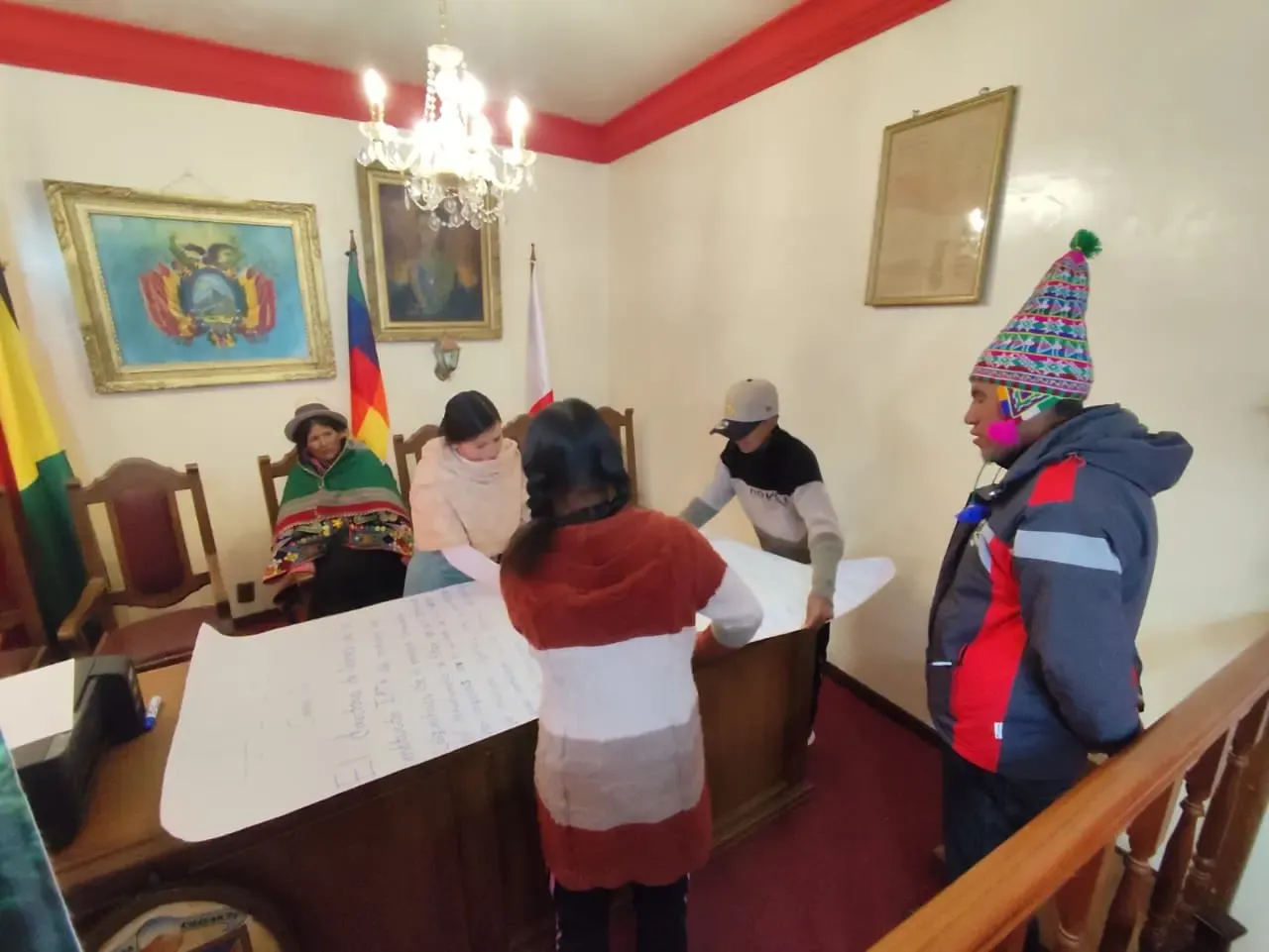 Grupo de comunarios, incluida una mujer con aguayo, elabora papelógrafos de trabajo en el salón municipal de Colquechaca