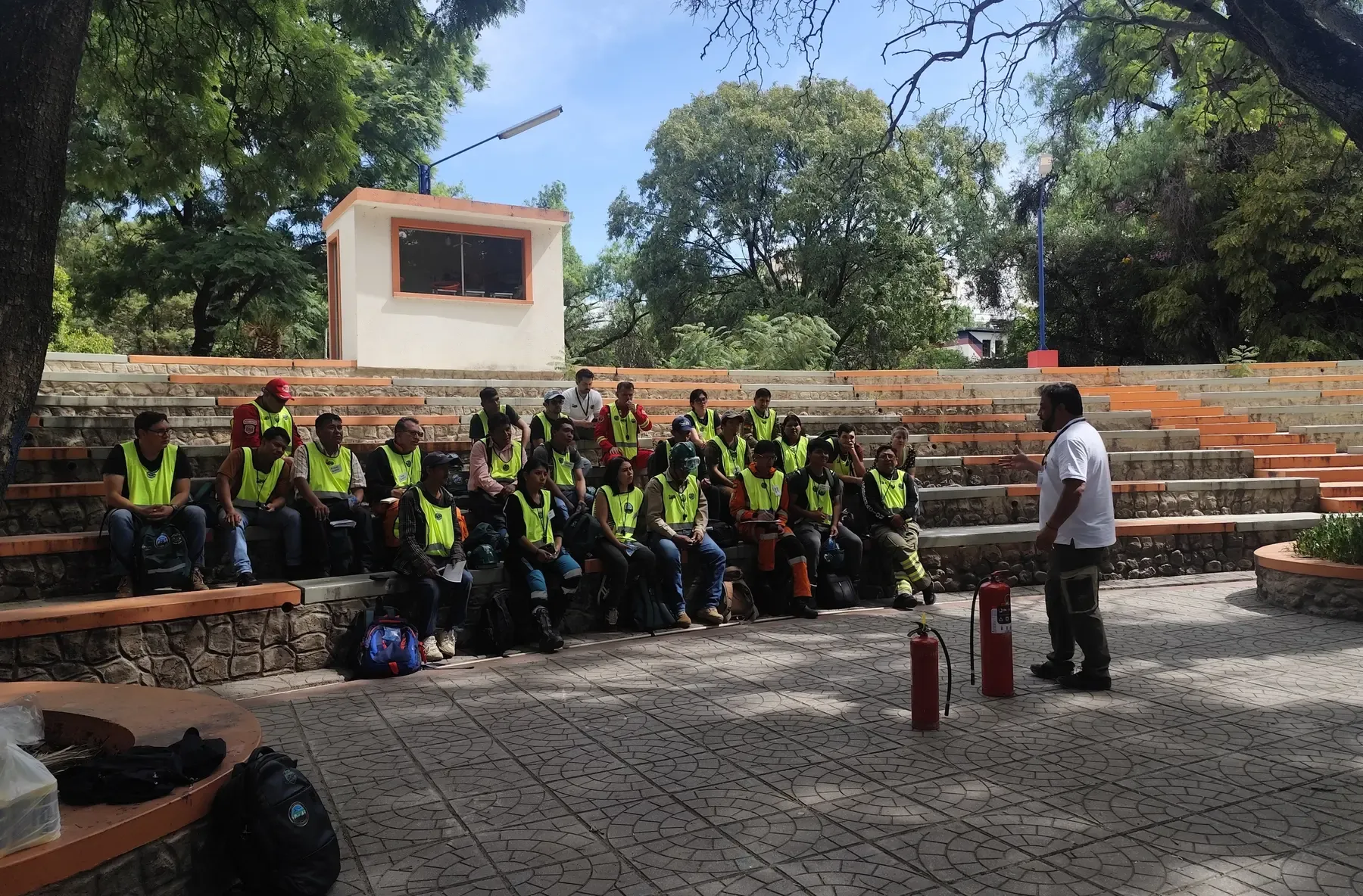 Vista amplia del anfiteatro con todos los participantes en chalecos amarillos frente al instructor y los extintores