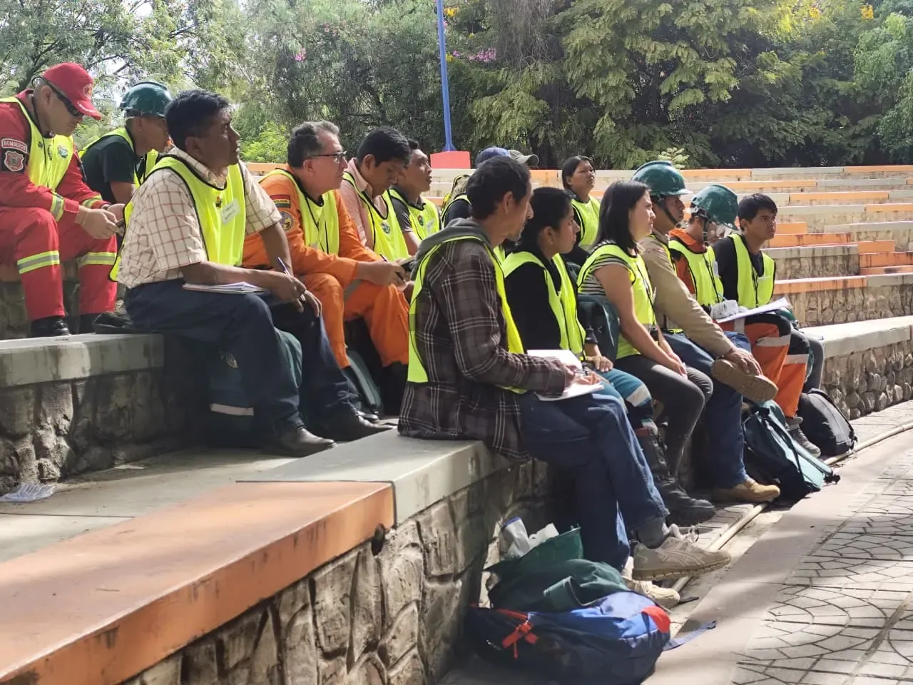 Fila de participantes con chalecos reflectivos, bombero de rojo y rescatista de naranja tomando apuntes en las gradas