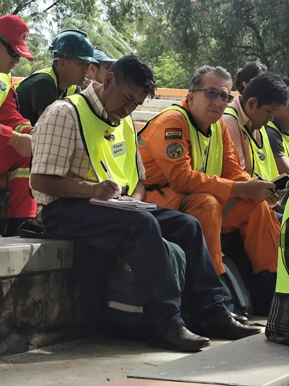 Voluntario con chaleco CERT y gafete escribe apuntes junto a rescatista con parche de Bolivia durante la capacitacion