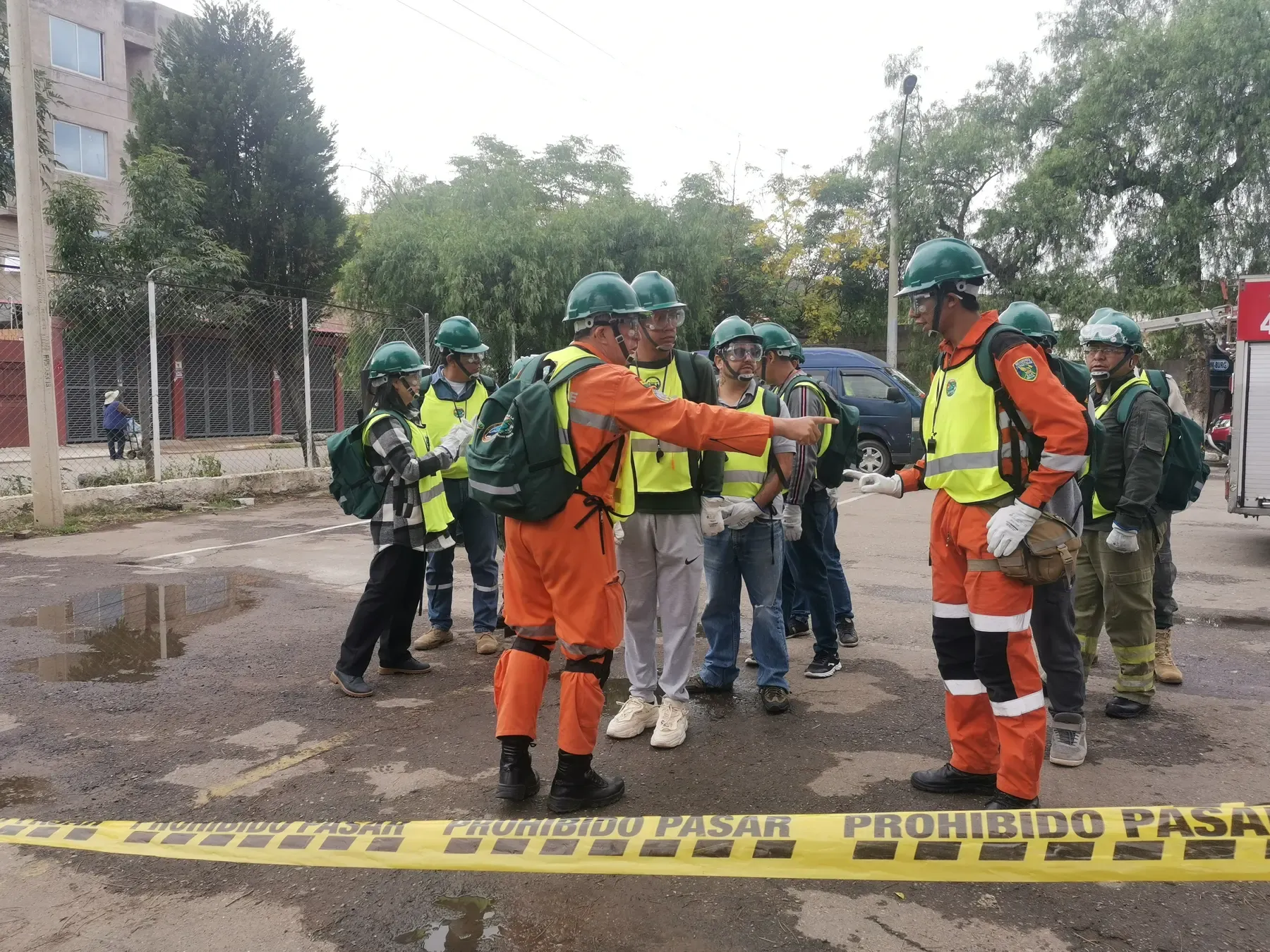 Tras la cinta PROHIBIDO PASAR, el lider de rescate de naranja asigna tareas a la escuadra de cascos verdes en plena via